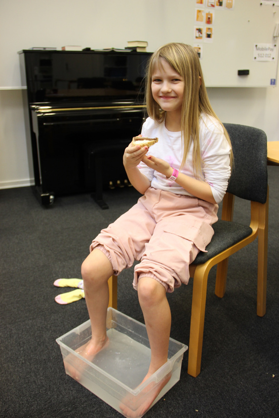 Pige smiler med fødderne i vand, holder et lille bagværk.