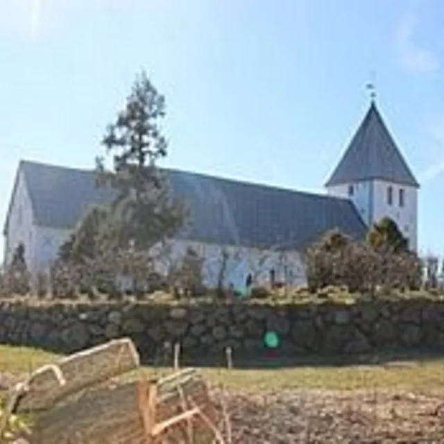 Hvid kirke med gråt tag og spir, bag en stenmur.