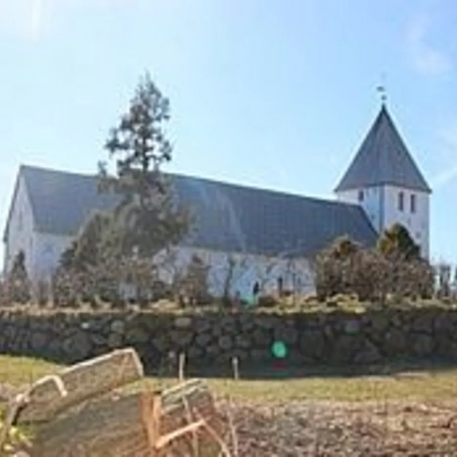 Hvid kirke med gråt tag og spir, bag en stenmur.