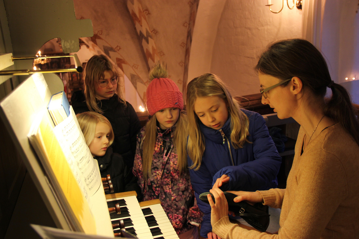 Kvinde og børn ved et kirkeorgel, kigger på en enhed.