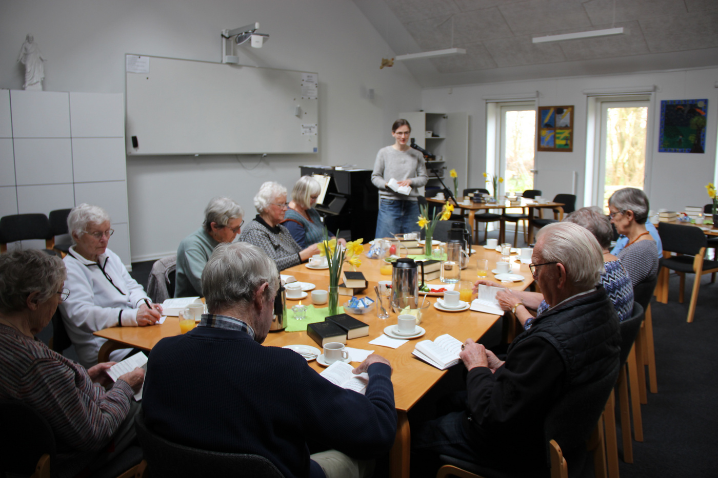  Gruppe ældre voksne læser omkring et bord, person står.