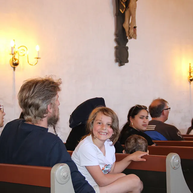 En ung pige smiler fra en kirkebænk under en gudstjeneste.