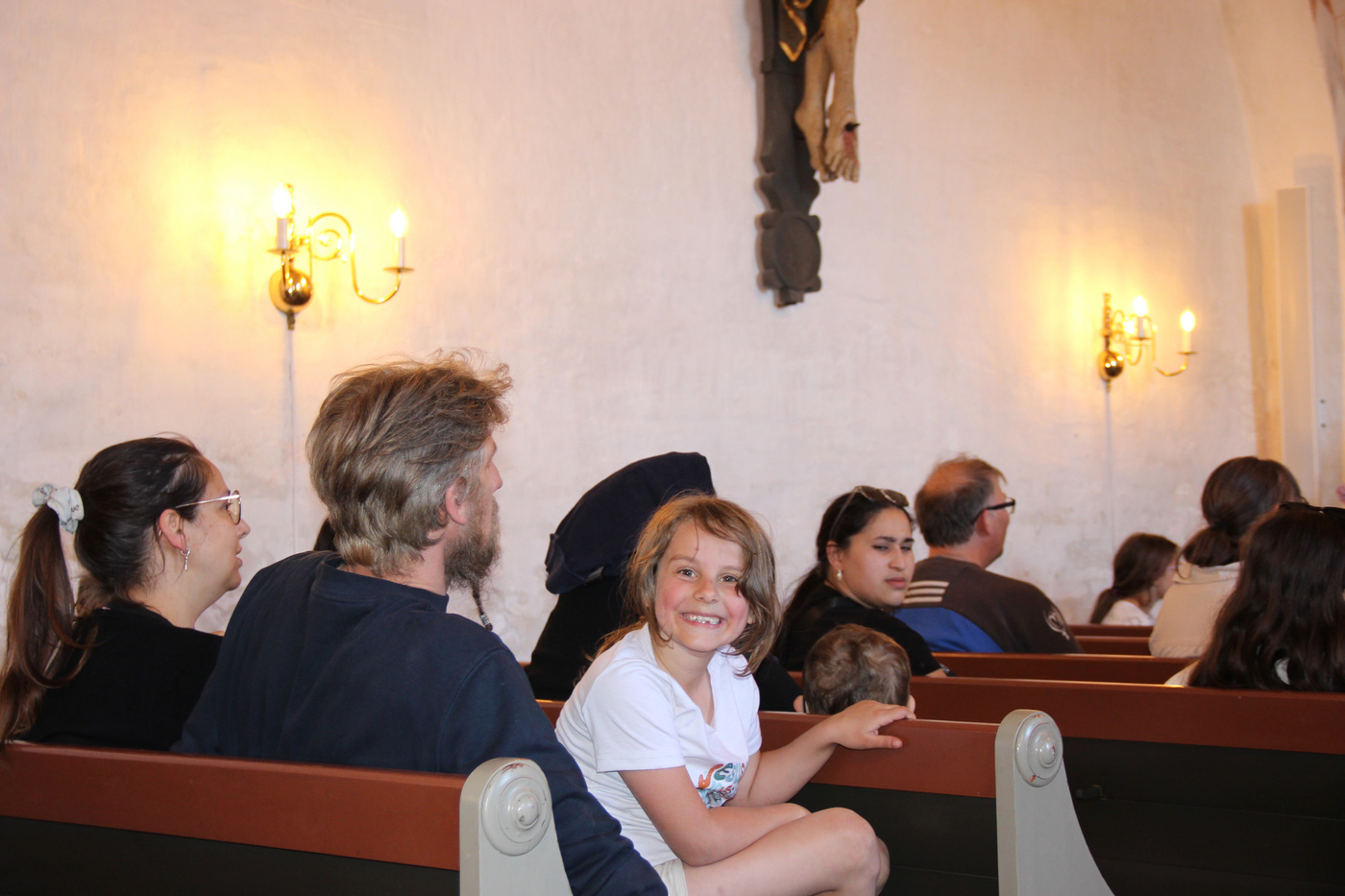 En ung pige smiler fra en kirkebænk under en gudstjeneste.