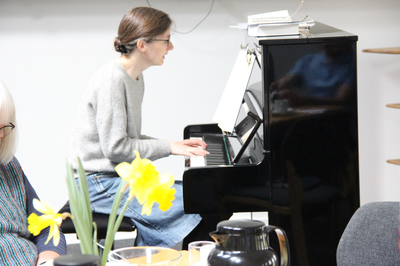 Person spiller klaver, med påskeliljer og kaffekande i forgrunden.