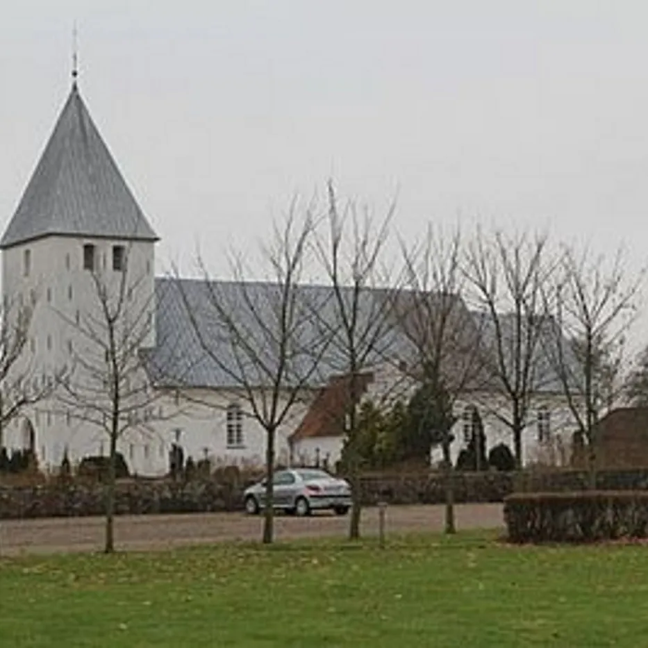 Hvid kirke med gråt tag og spir, omgivet af nøgne træer.