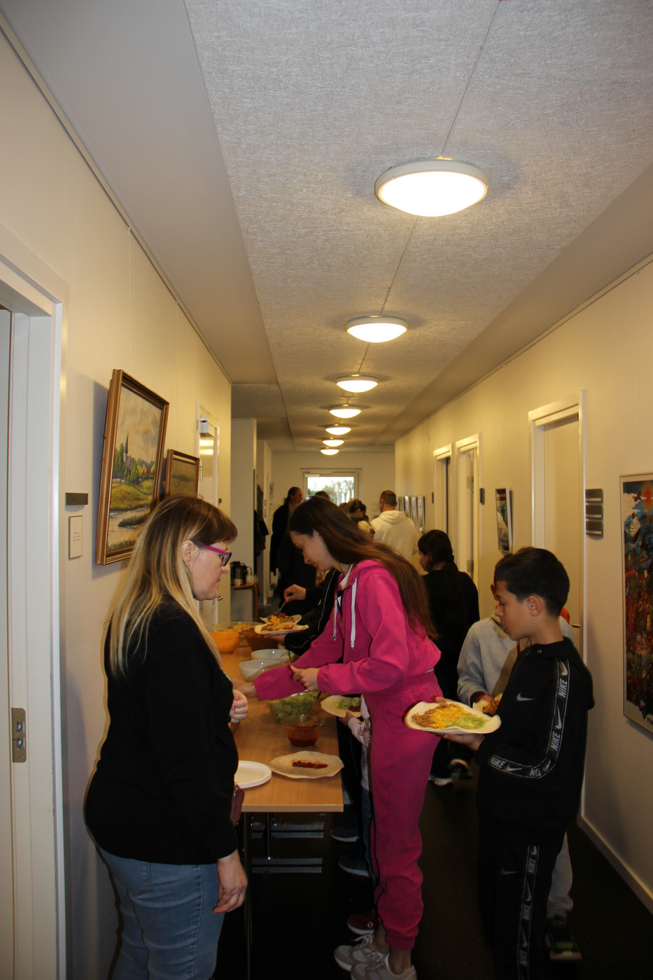 Folk i kø og forsyner sig med mad fra et bord i en gang.