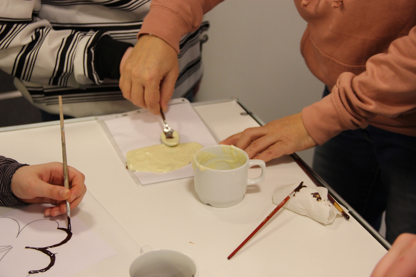 Hænder spreder smeltet hvid chokolade, maler et design i nærheden.