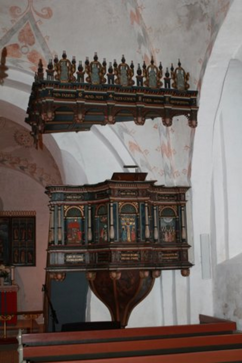 Udsmykket træprædikestol med malede paneler og baldakin.