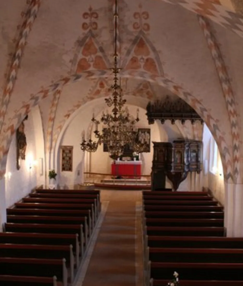 Kirkeinteriør med mønstret loft, kirkebænke, alter og lysekroner.