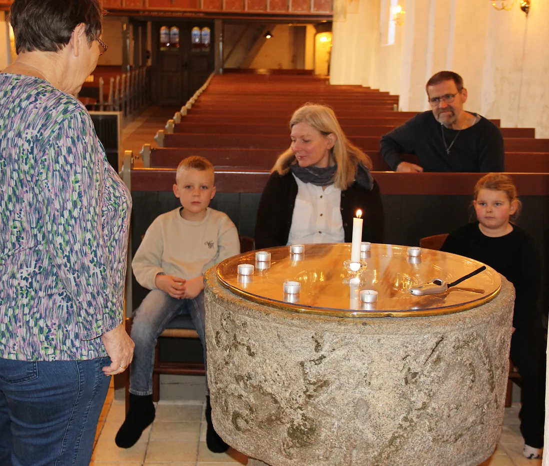 Familie samlet omkring en stor stenfont med levende lys i kirken.