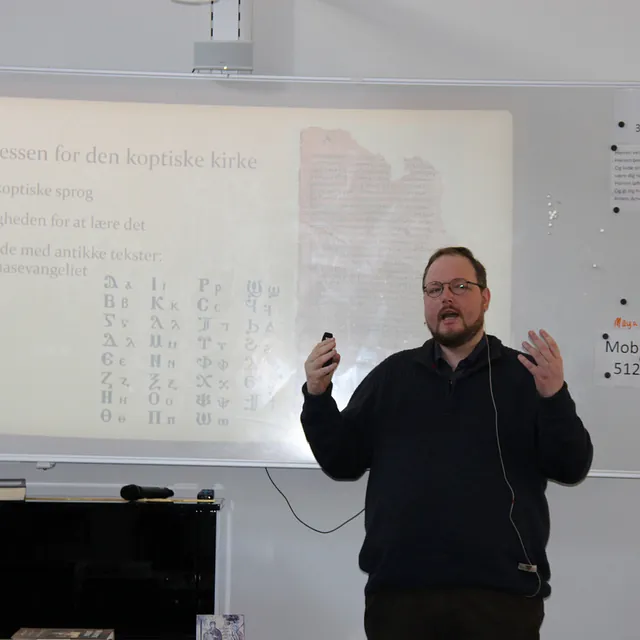 Mand med briller præsenterer om koptisk sprog på en whiteboardtavle.