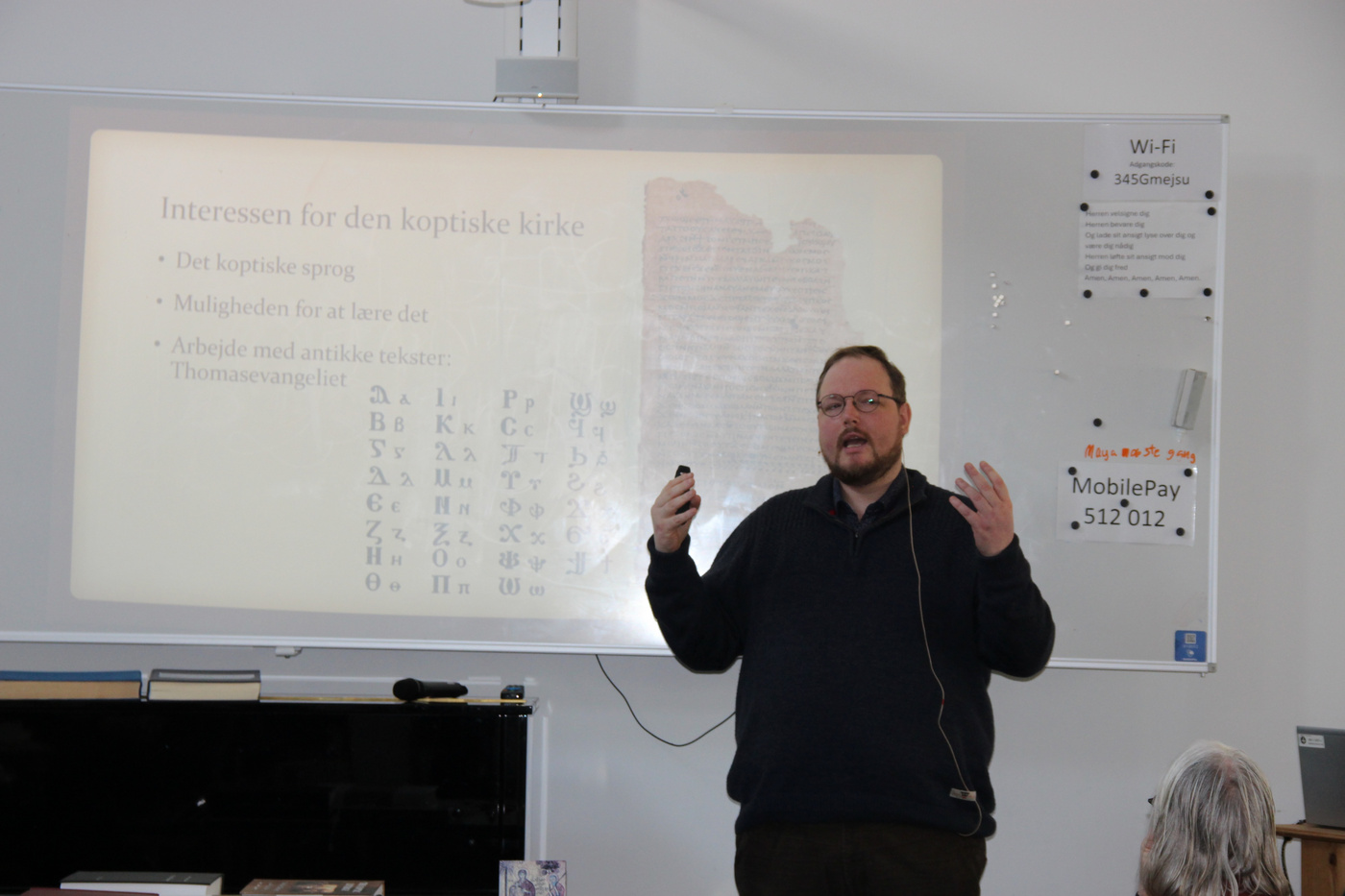 Mand med briller præsenterer om koptisk sprog på en whiteboardtavle.