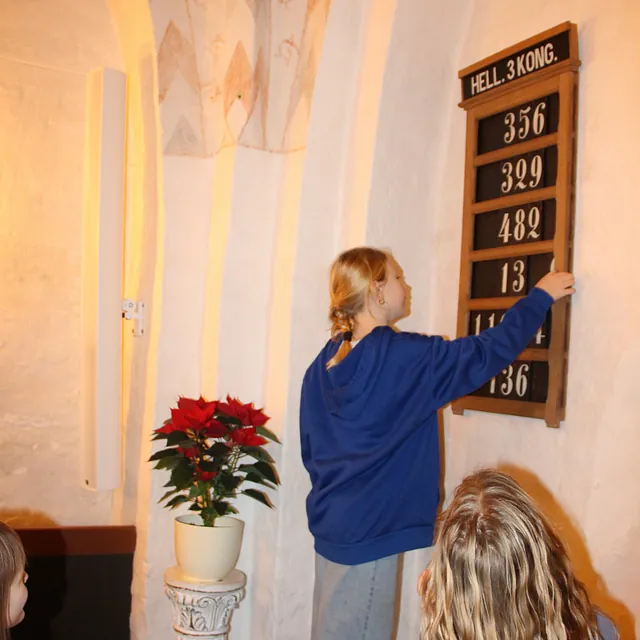 Pige justerer numre på en salmetavle i en kirke.
