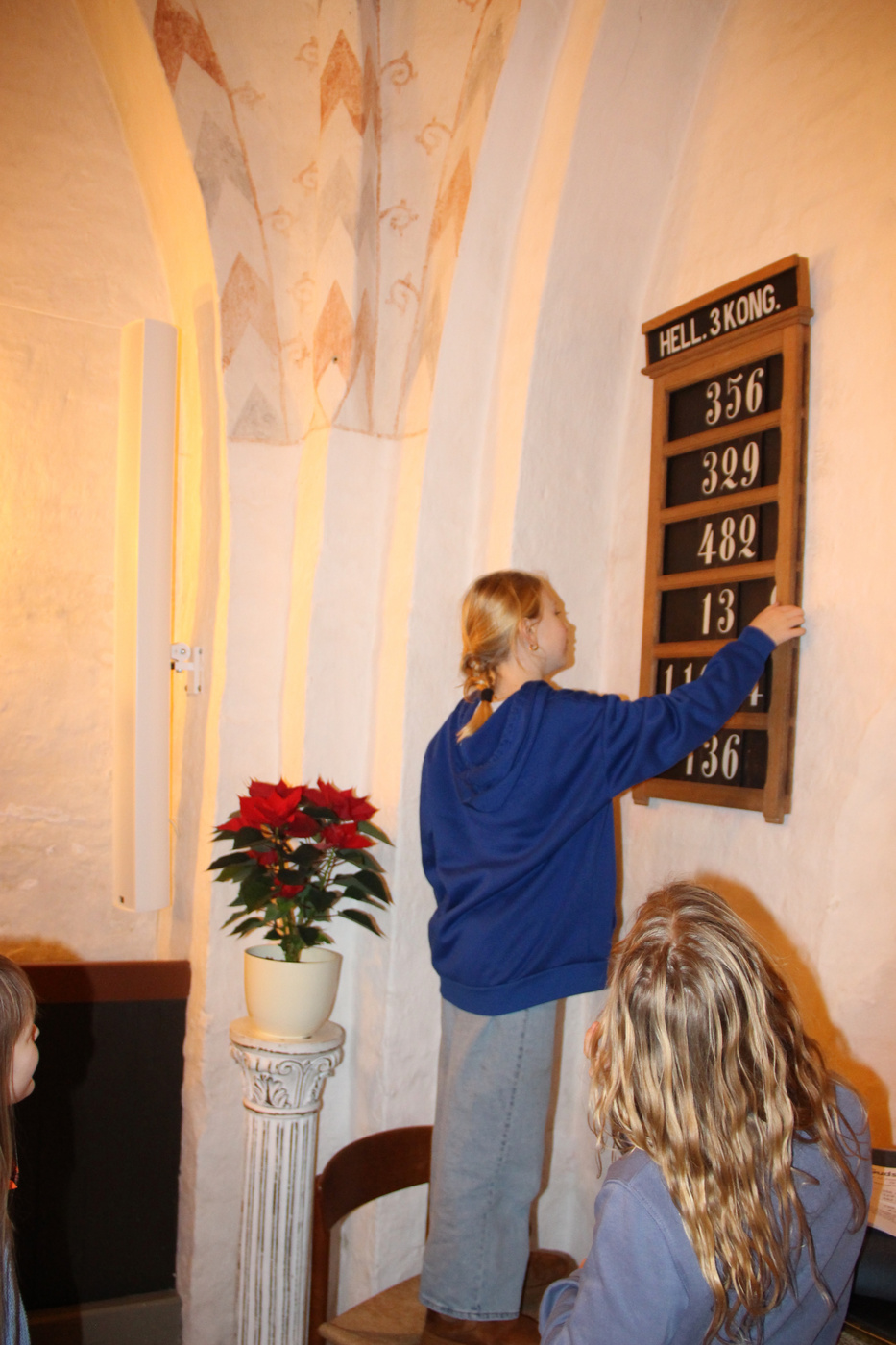 Pige justerer numre på en salmetavle i en kirke.