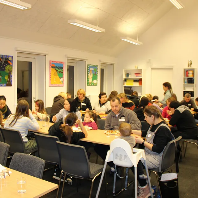 Familier og enkeltpersoner sidder ved borde, spiser og hygger.