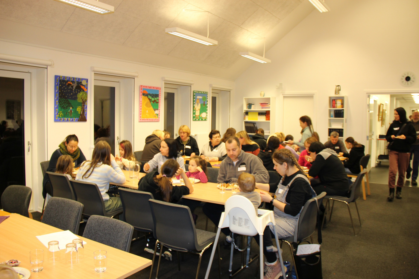 Familier og enkeltpersoner sidder ved borde, spiser og hygger.