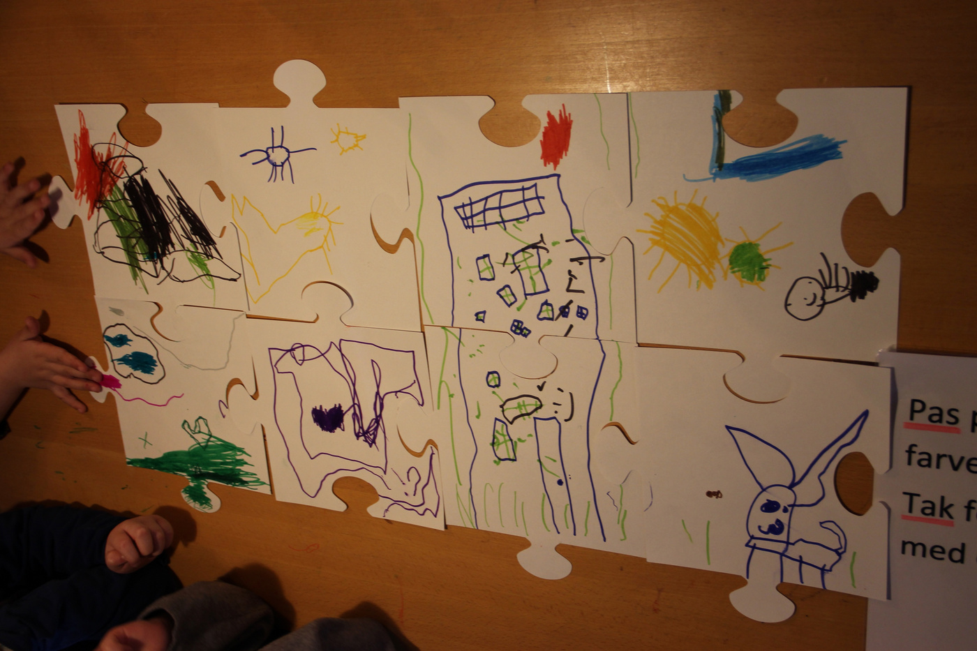 Børnetegninger samlet på store puslespilsbrikker på gulvet.