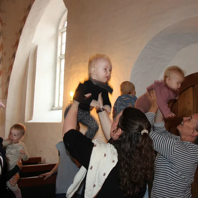 Voksne løfter glædeligt babyer op i luften i en kirke.