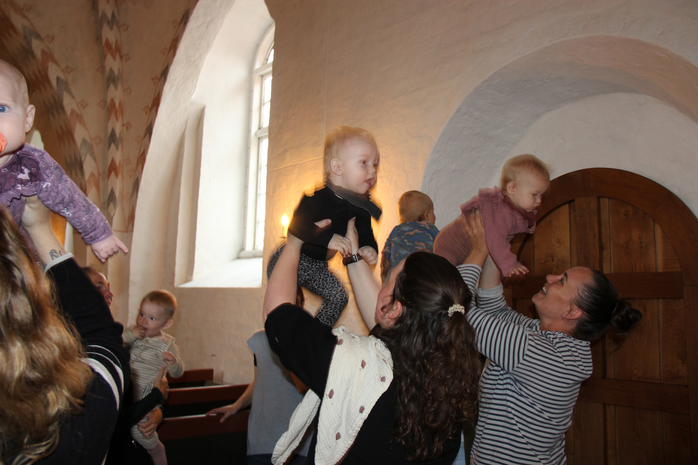 Voksne løfter glædeligt babyer op i luften i en kirke.