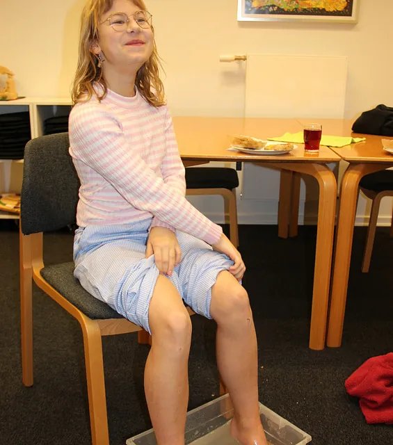 Pige med briller smiler, fødderne i et bassin med vand.