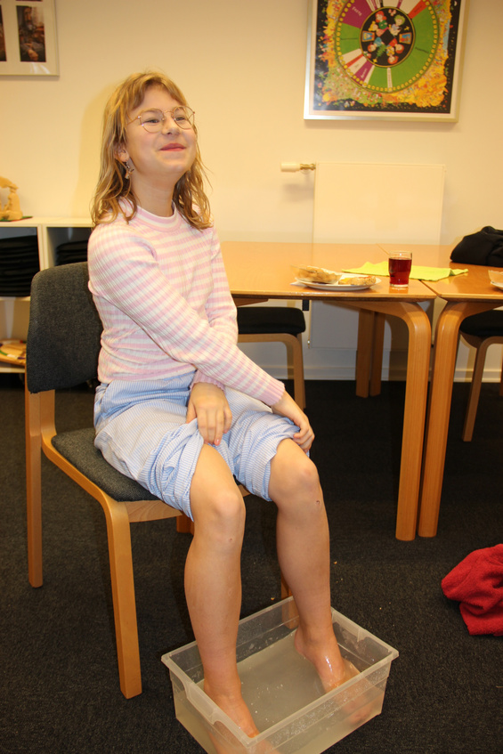 Pige med briller smiler, fødderne i et bassin med vand.