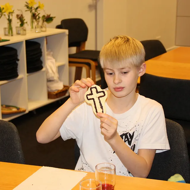 Dreng holder en korsformet småkage med et chokoladekors.