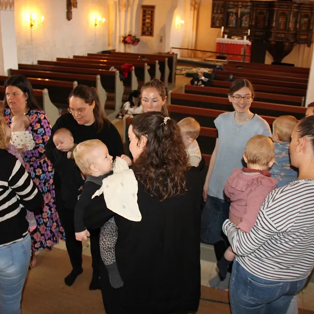 Flere kvinder med babyer socialiserer i en kirke.