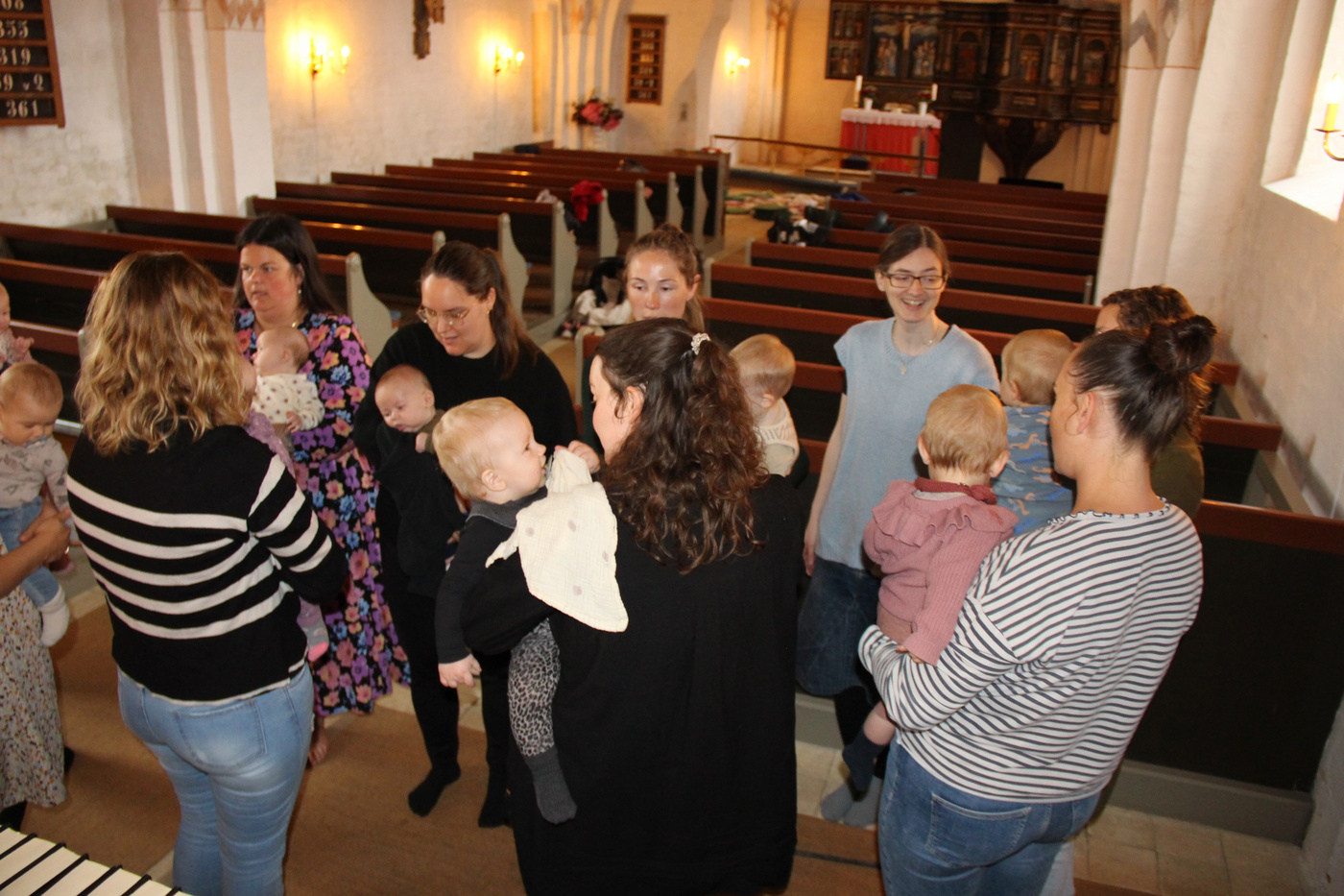Flere kvinder med babyer socialiserer i en kirke.