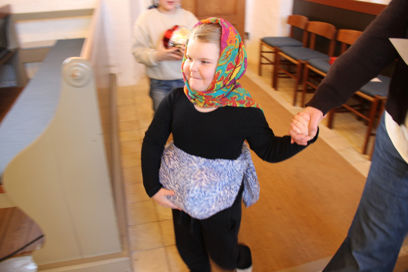 Barn i farverigt tørklæde og bæresele holder en voksens hånd.