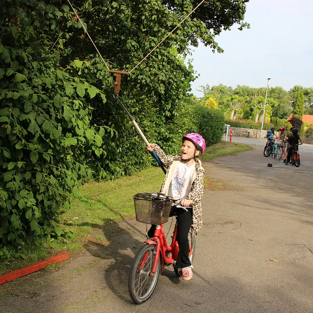 Pige på blå cykel, med hjelm, rækker ud efter et ophængt mål.