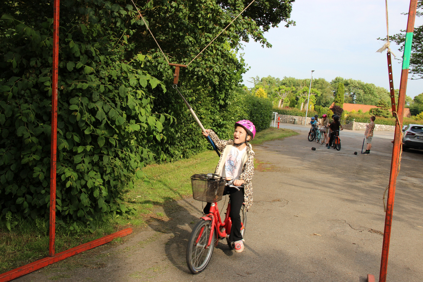Pige på blå cykel, med hjelm, rækker ud efter et ophængt mål.