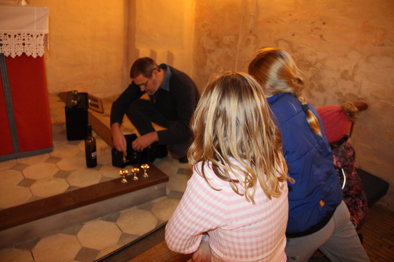 Mand arrangerer lys nær alter, to børn ser på fra kirkebænke.