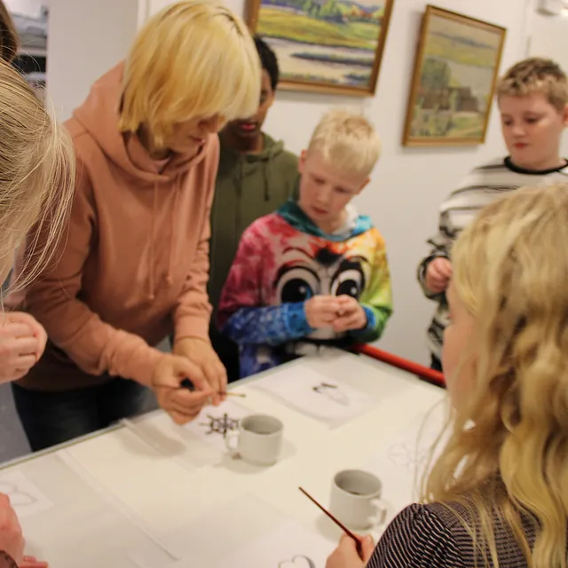  Voksne og børn samlet omkring et bord, engageret i en kreativ aktivitet.