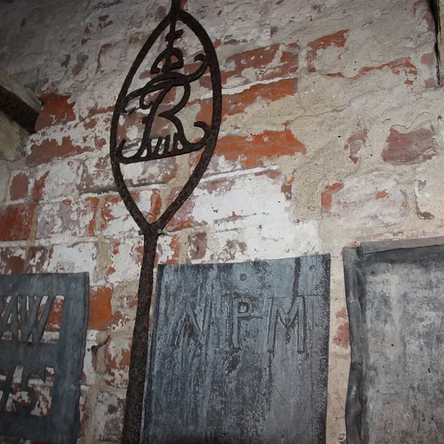 Gamle metalgravmæler mod en murstensvæg, med et dekorativt kors.