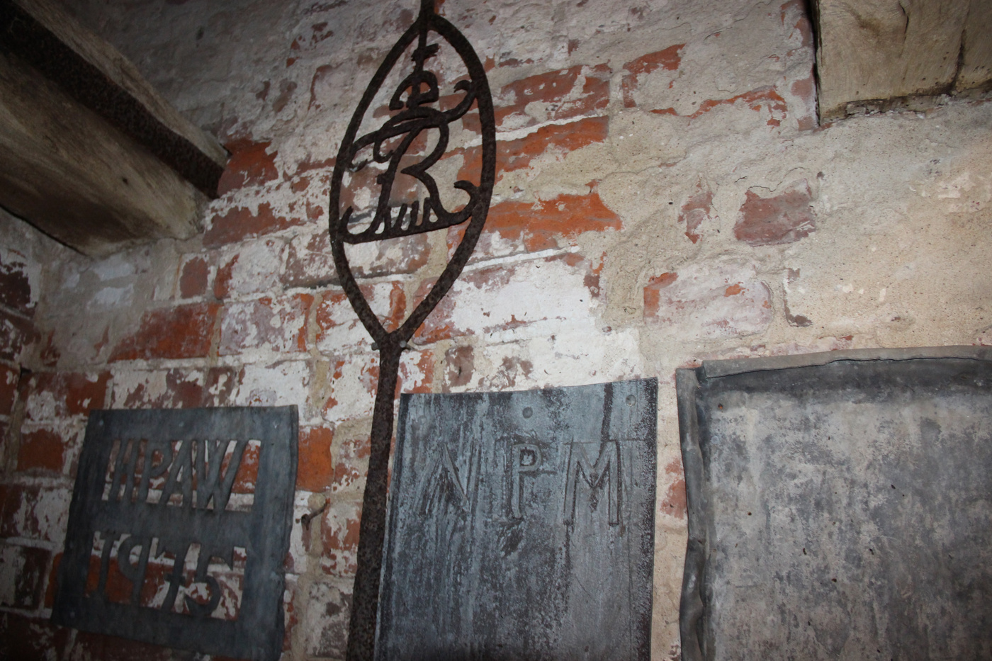 Gamle metalgravmæler mod en murstensvæg, med et dekorativt kors.