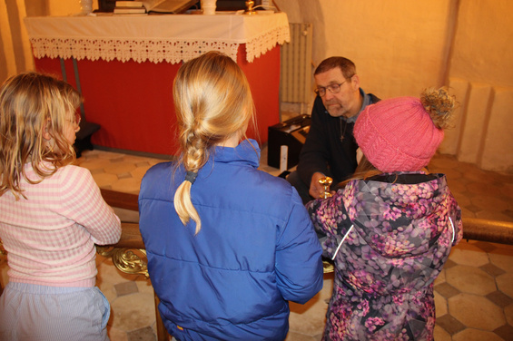 Mand ved alter taler til tre børn i kirken.