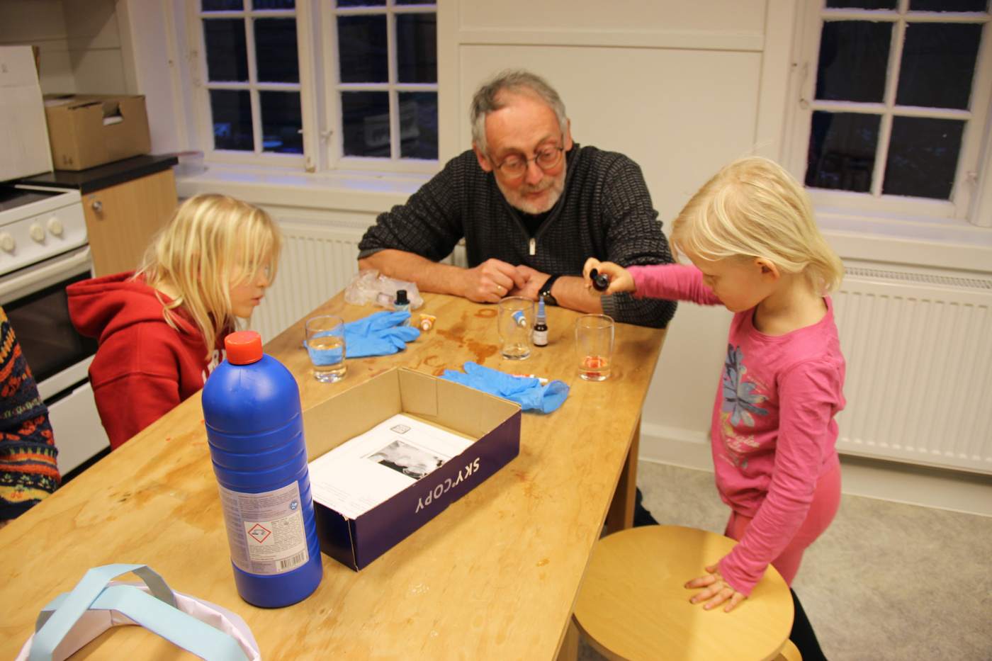 Voksen og to børn laver et videnskabeligt eksperiment ved et bord.