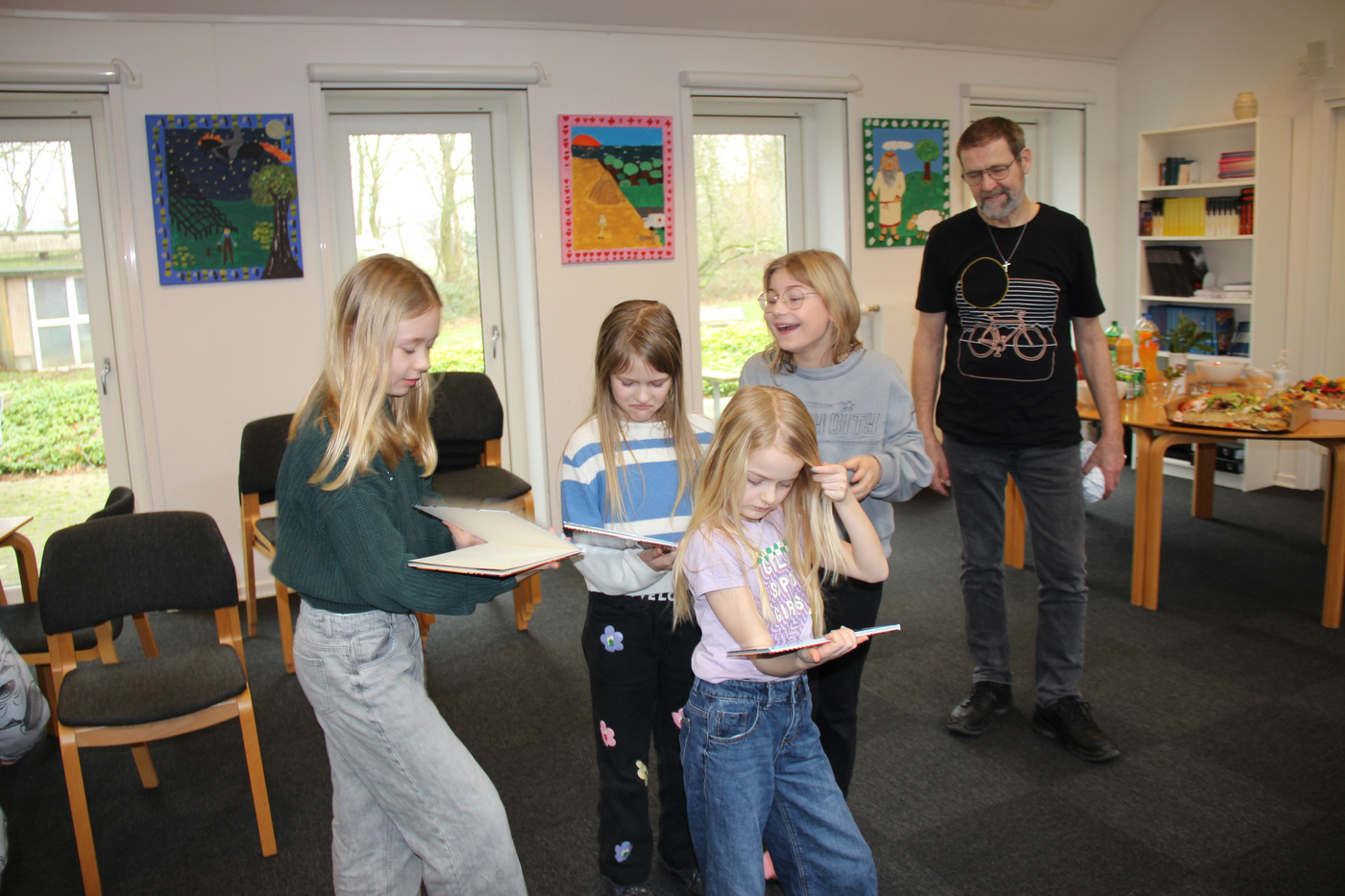 Fire piger og to voksne interagerer i et lyst rum.