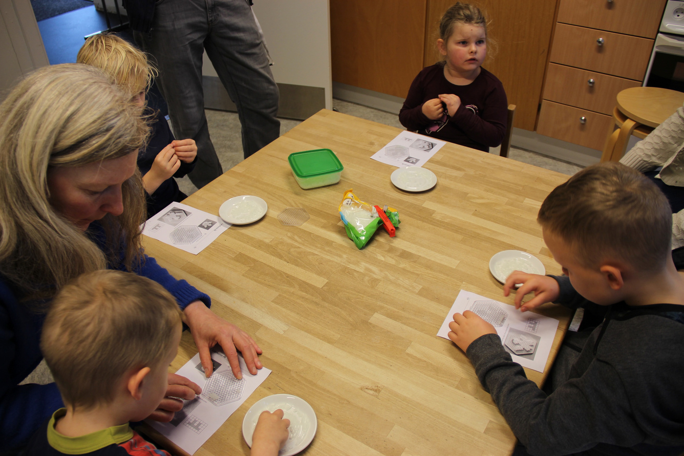 Voksen og børn sidder omkring et bord, engageret i en aktivitet.