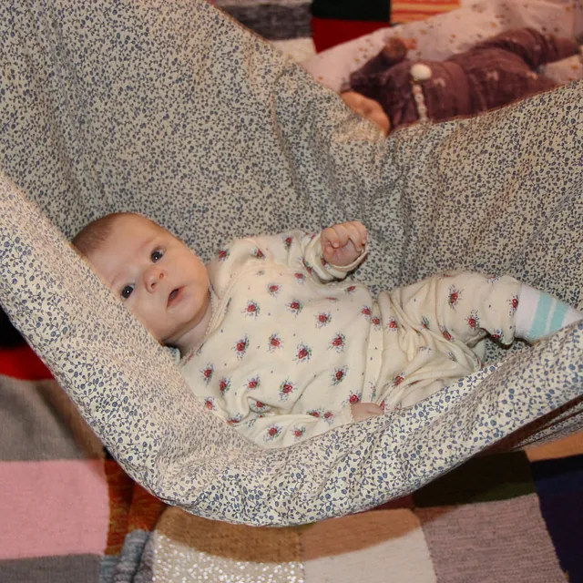 Baby ligger i en stofgynge, holdt af to voksne.