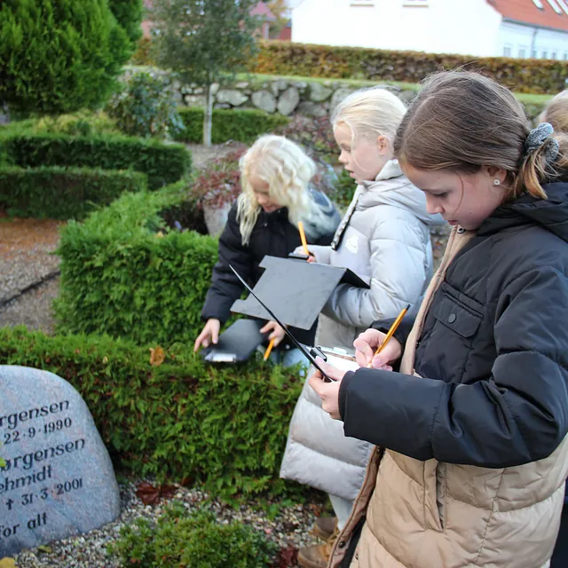 Børn tegner eller skriver ved gravsten på en kirkegård.
