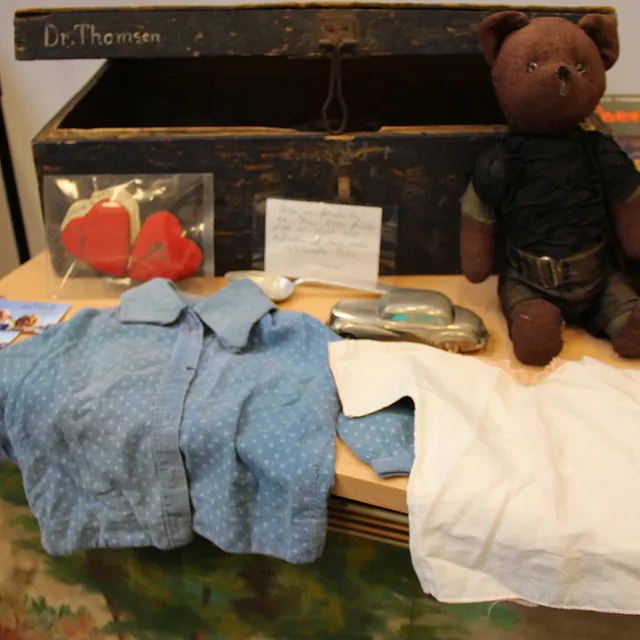 Samling af vintage genstande: bamse, tøj og en gammel trækasse.