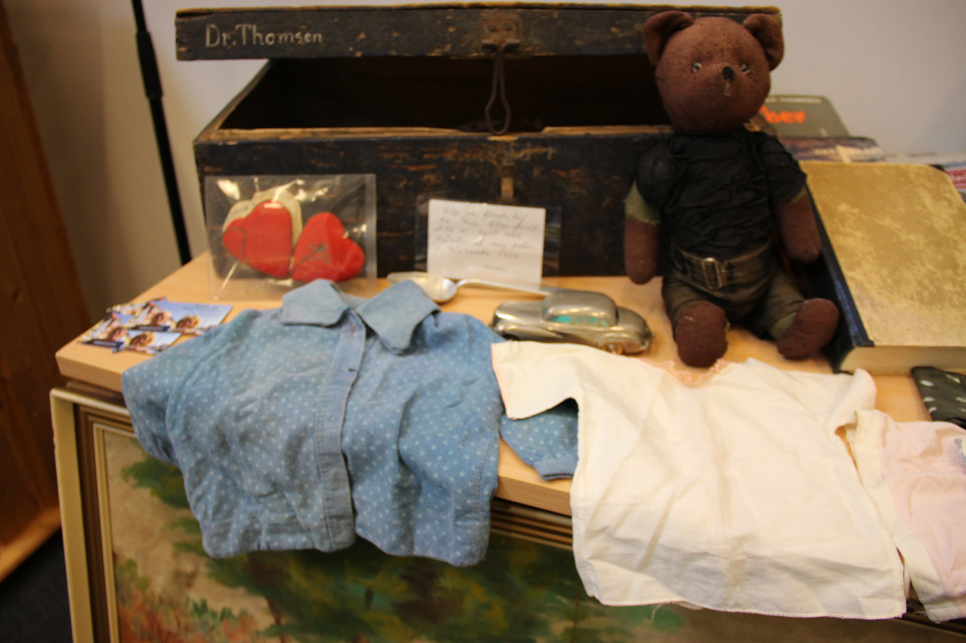 Samling af vintage genstande: bamse, tøj og en gammel trækasse.