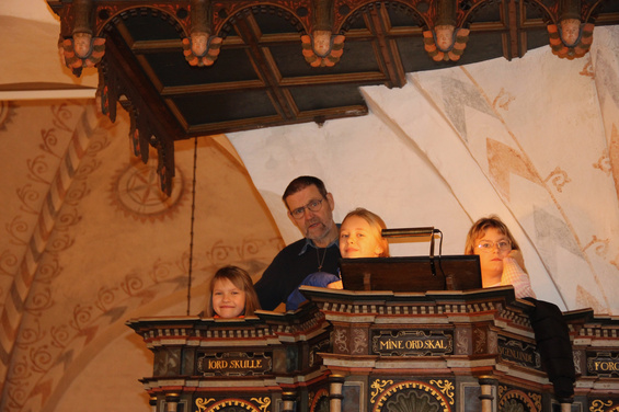 Mand og tre børn i en udsmykket kirkeprædikestol.