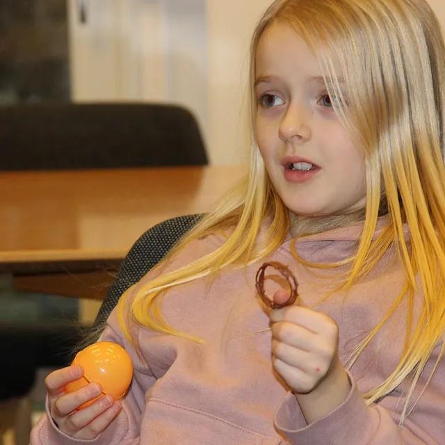 Pige holder et orange æg og en chokoladekonfekt, ser overrasket ud.