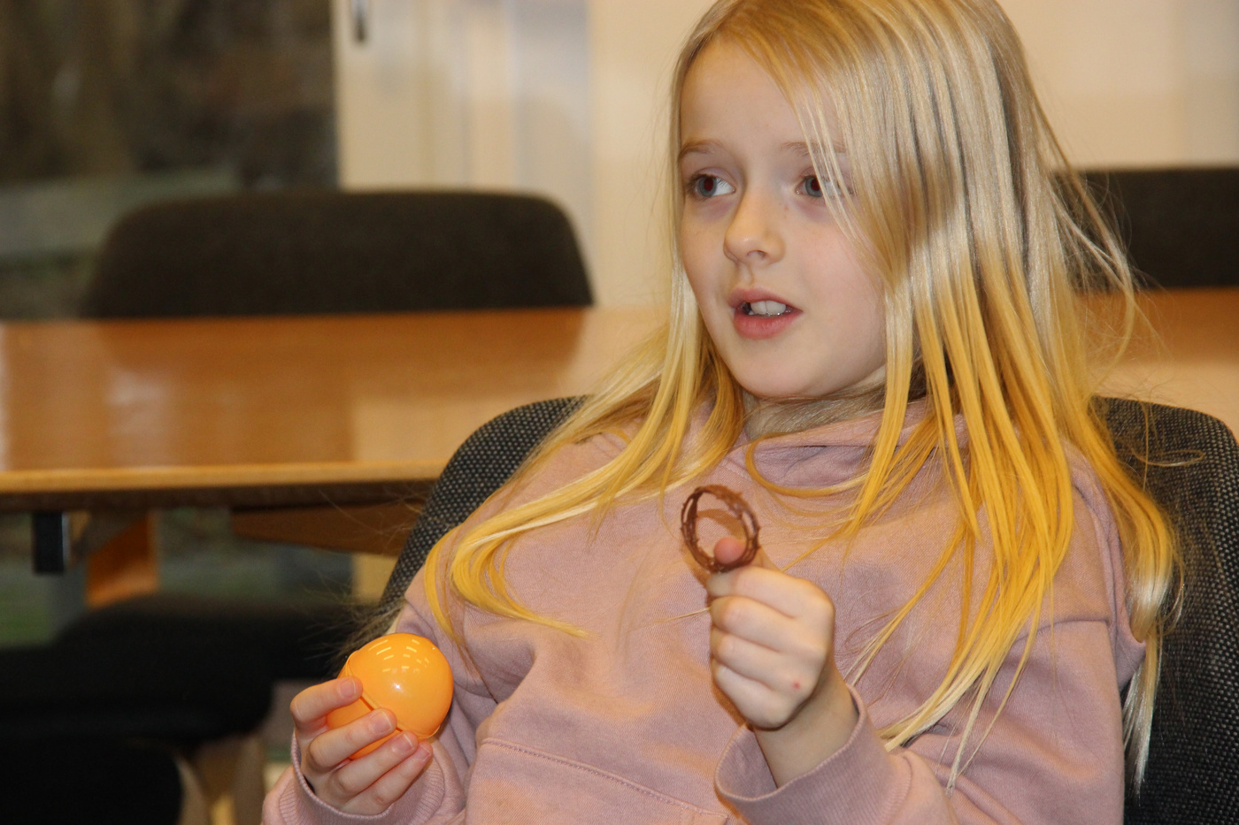 Pige holder et orange æg og en chokoladekonfekt, ser overrasket ud.