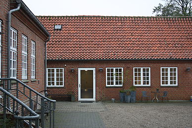 Rød murstensbygning med hvide vinduer og rødt tegltag.