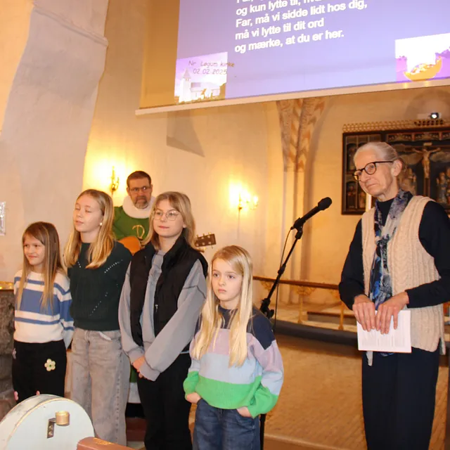 Børn og voksne står i en kirke med projicerede salmetekster.