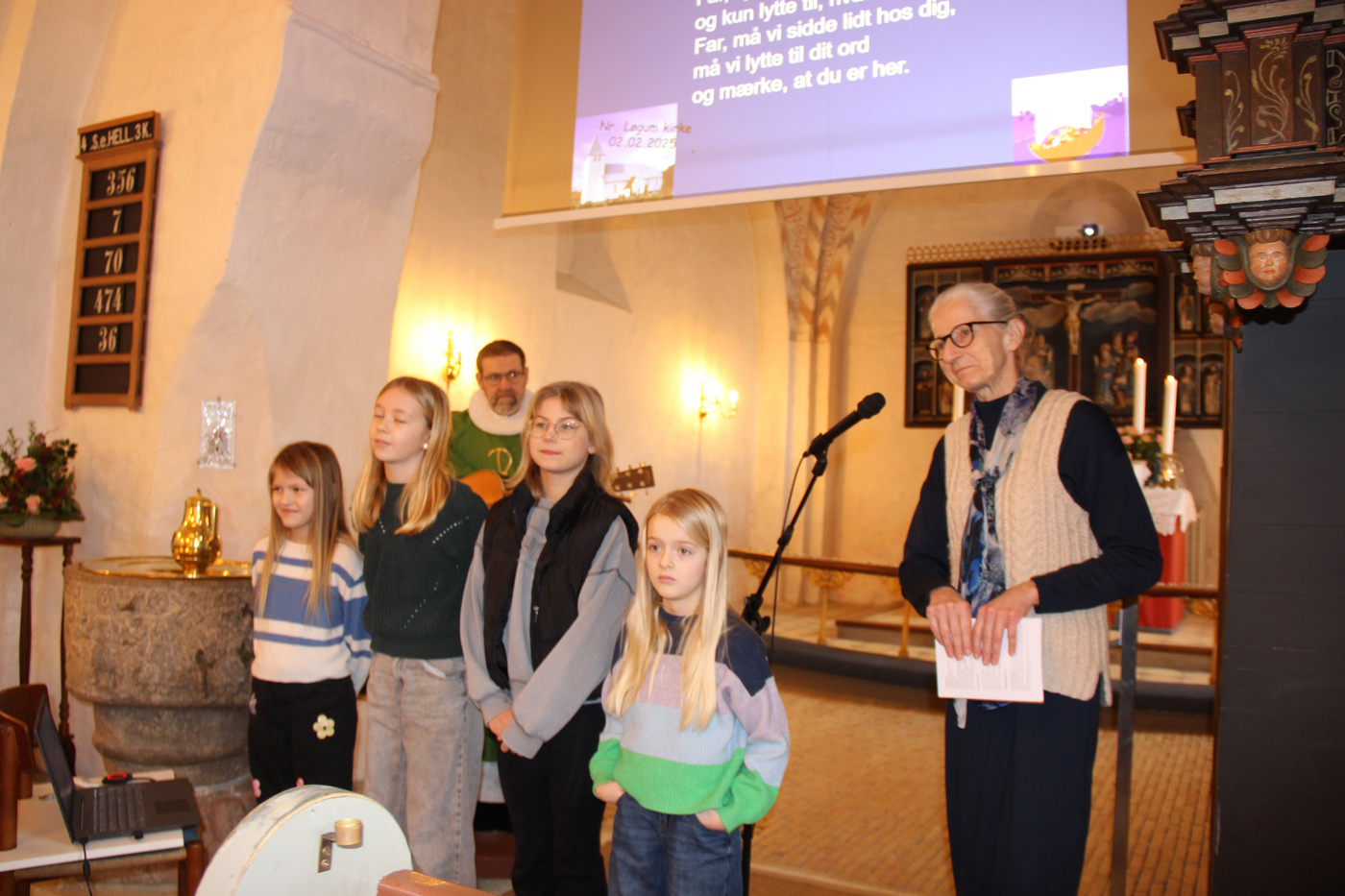 Børn og voksne står i en kirke med projicerede salmetekster.
