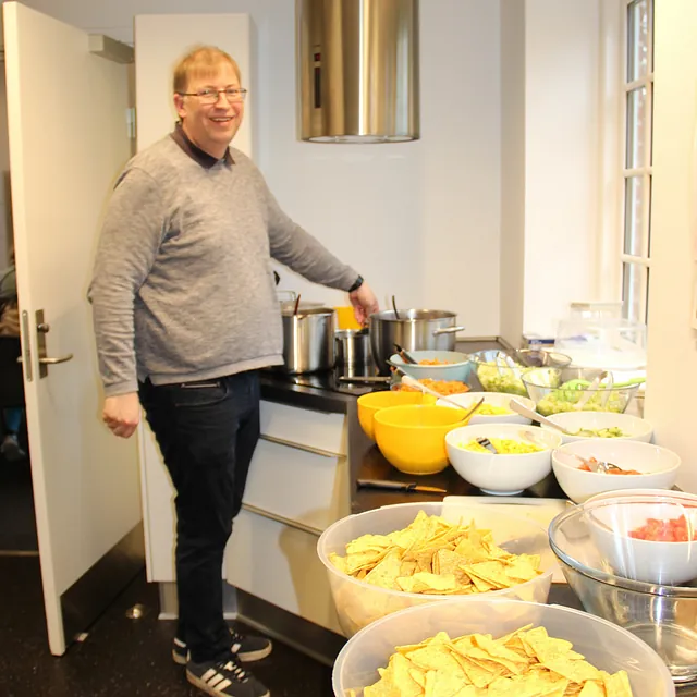 Mand står ved en buffet med skåle af chips og salater.